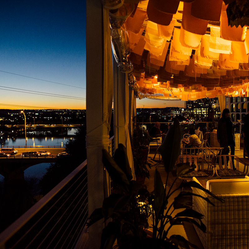 The terrace is decorated with lights and small flags, and people are enjoying their drinks in the dim lighting.