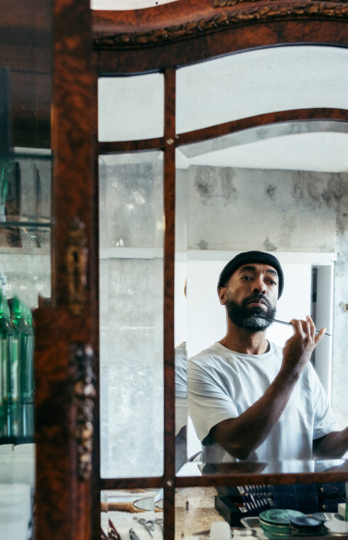 A man in a white tee delicately combs his beard, gazing into the mirror attentively.