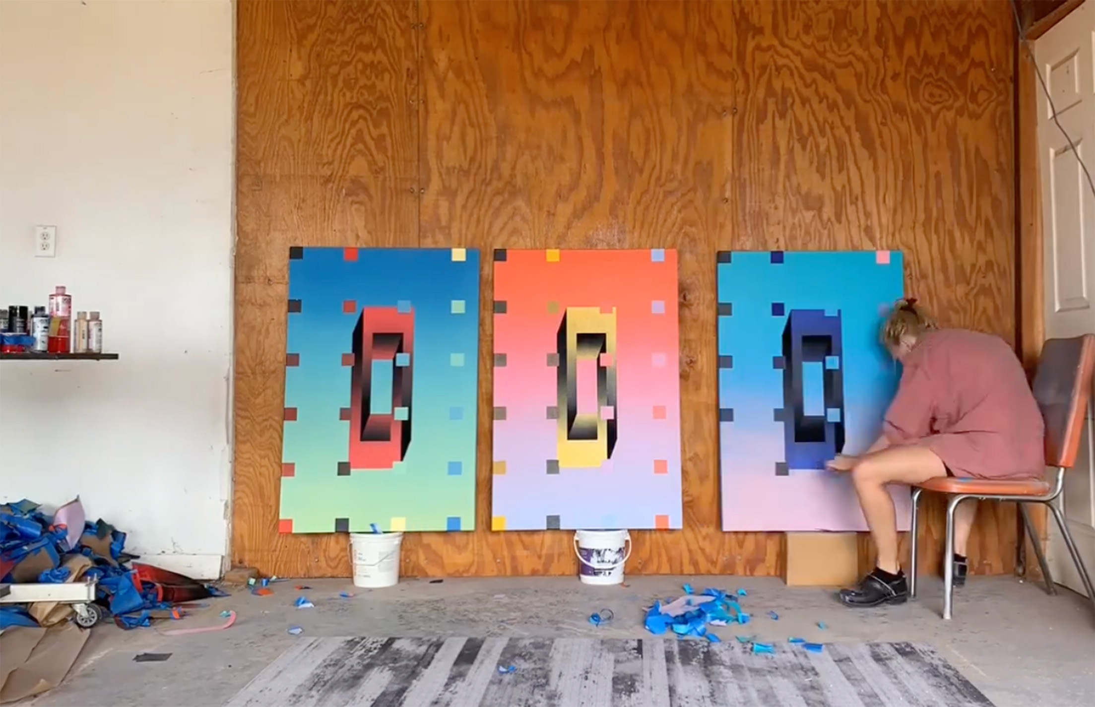 A man seated on a chair, creating artwork on cardboard.