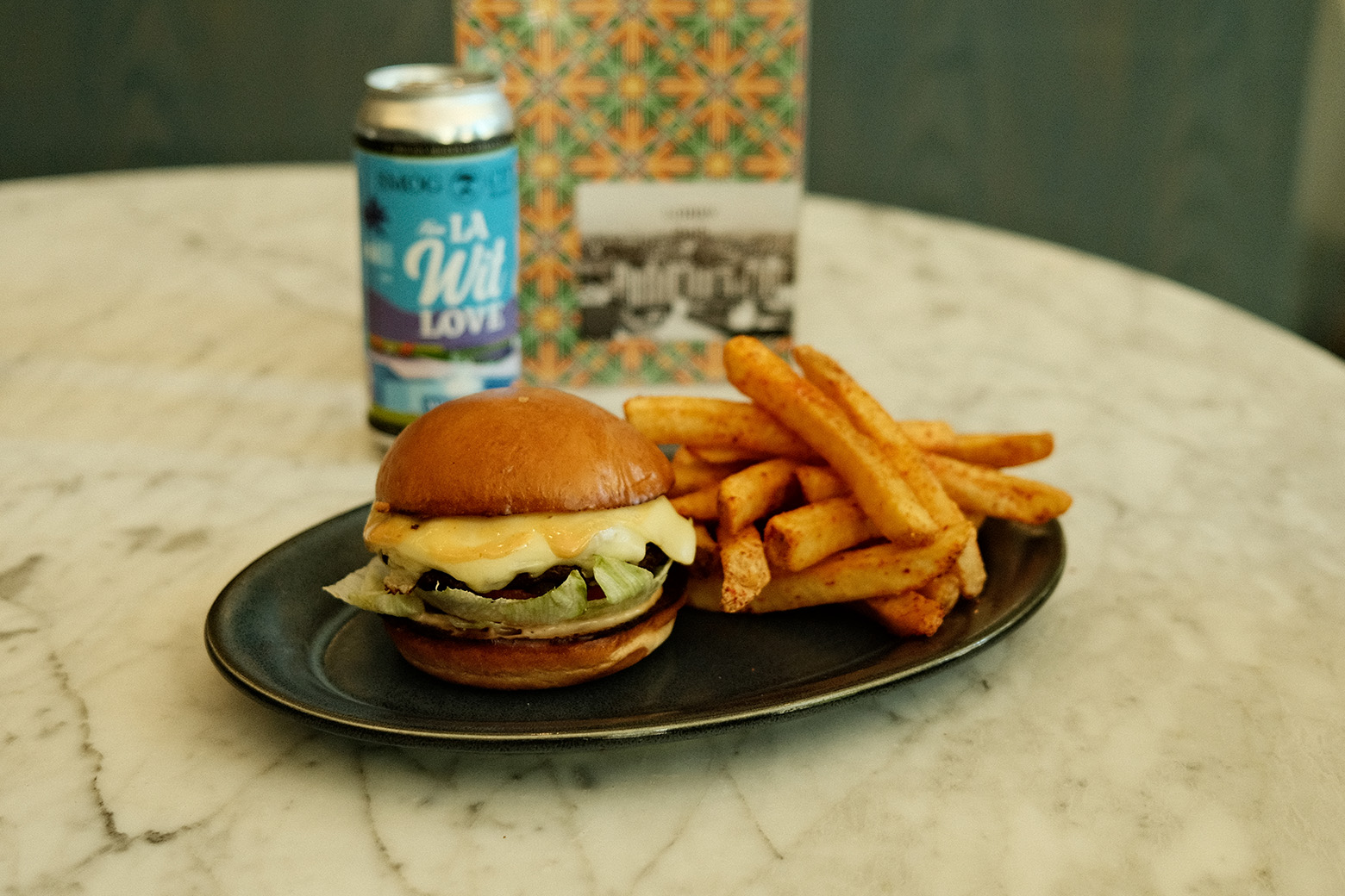 a can of beer next to a plate of burger with fries