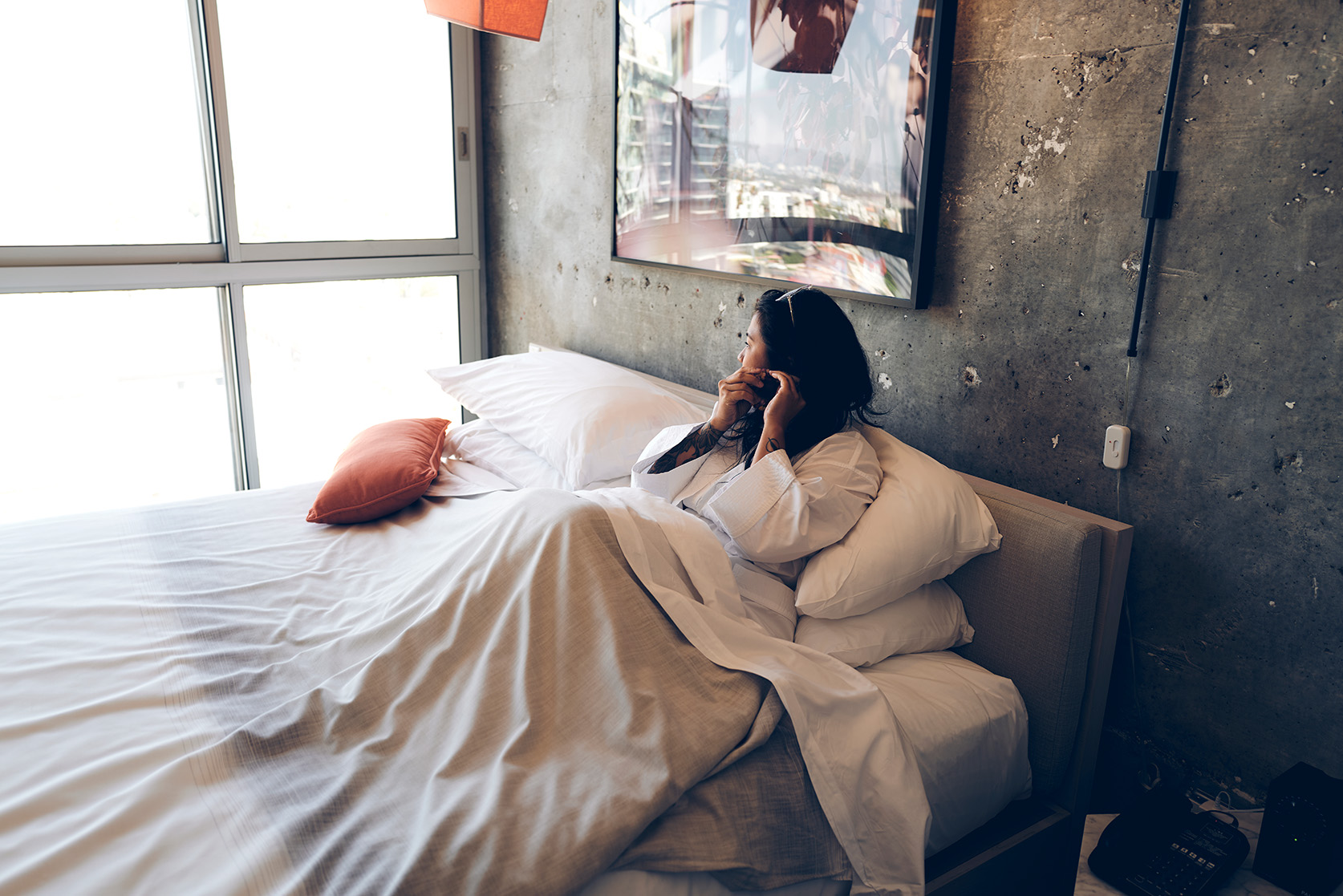 a woman in bathrobe looking out the window while sitting in bed