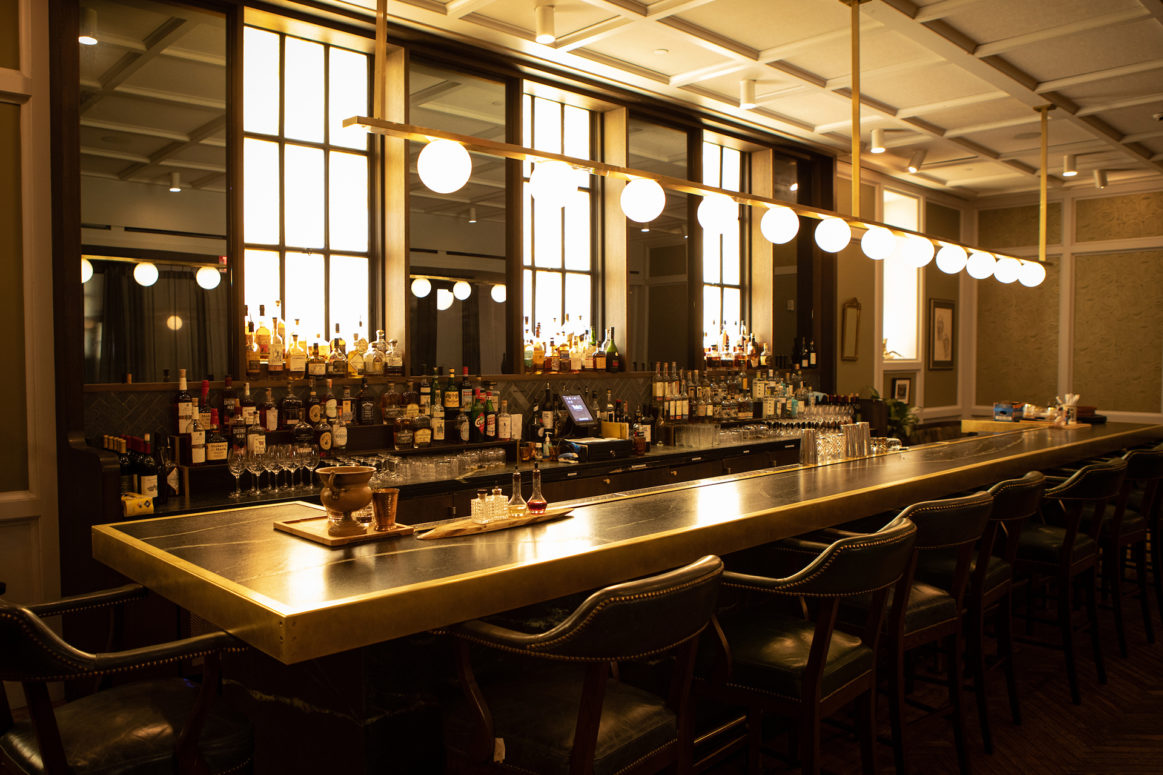 Picture of a big dining table withglasses on near the bar counter along with lights on the top