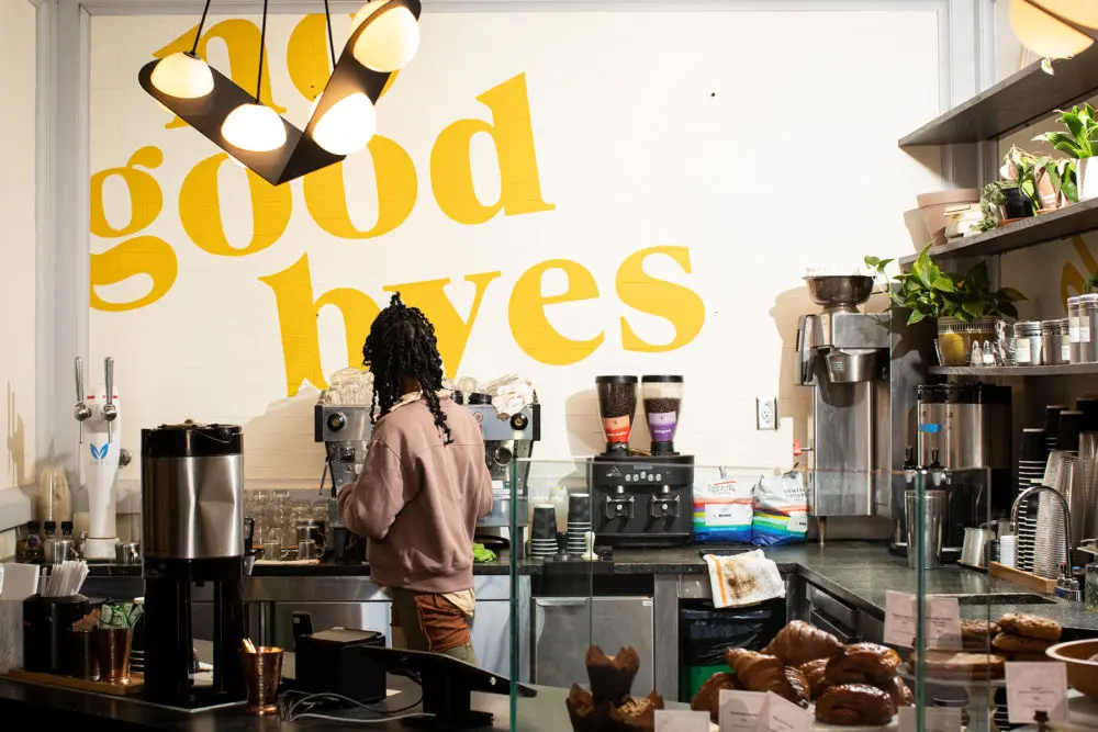 Picture of a kitchen where a person with curly hairs is looking towards the machine along with no good byes on wall