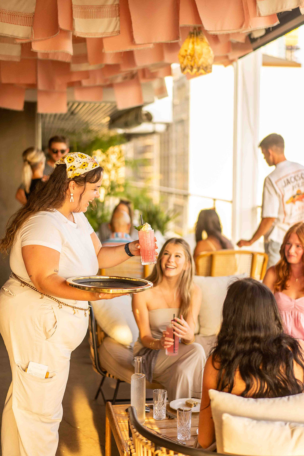 A waitress serving a drink to a group of people sitting outdoor on a rooftop