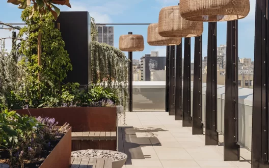 A rooftop sitting area with hanging lamps and lush green planted trees.